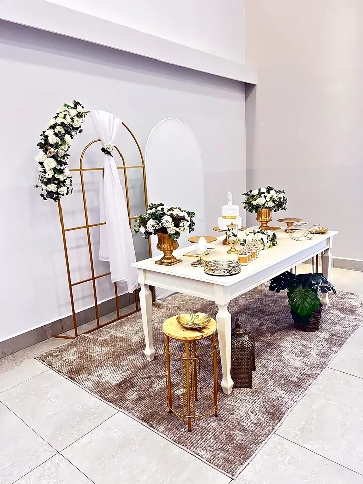 Mesa branca com arco dourado e arranjos de flores brancas