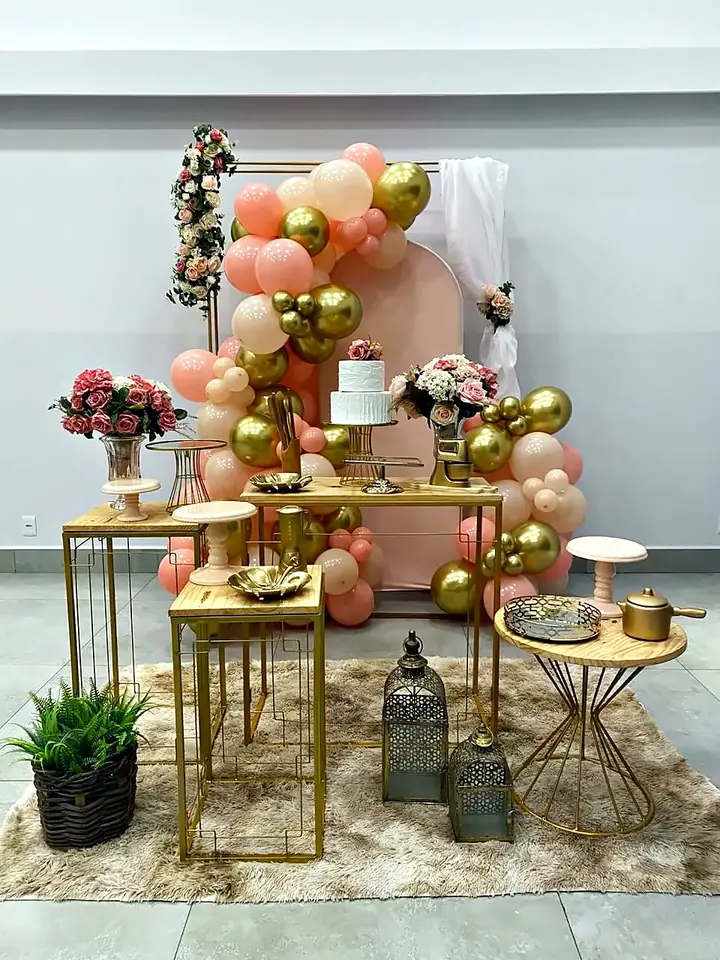 Mesa rosé e dourada com arco de flores e lanternas